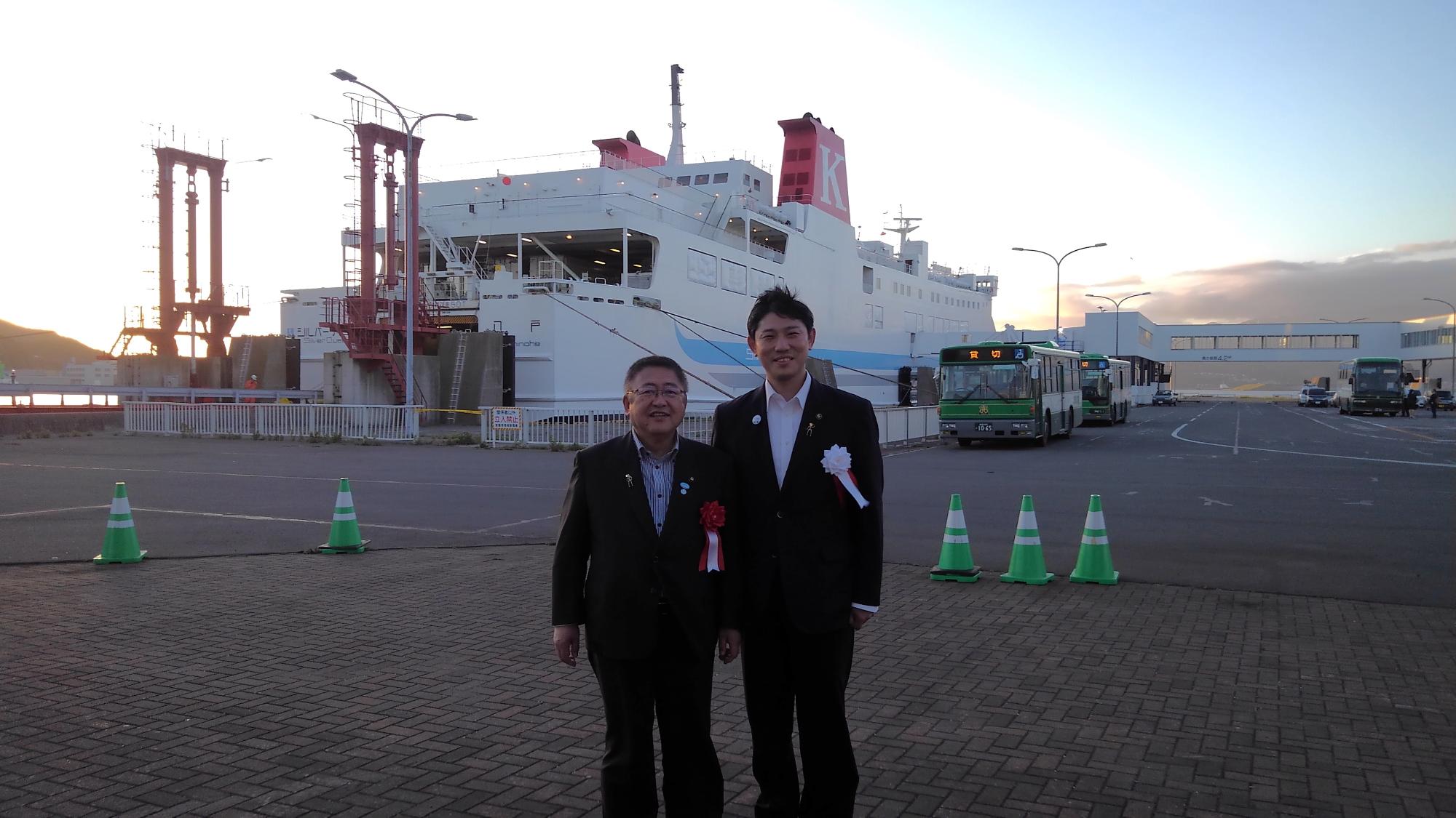 船が停泊する港で、胸章をつけた市長と室蘭市の青山剛市長が並んで立つ記念写真