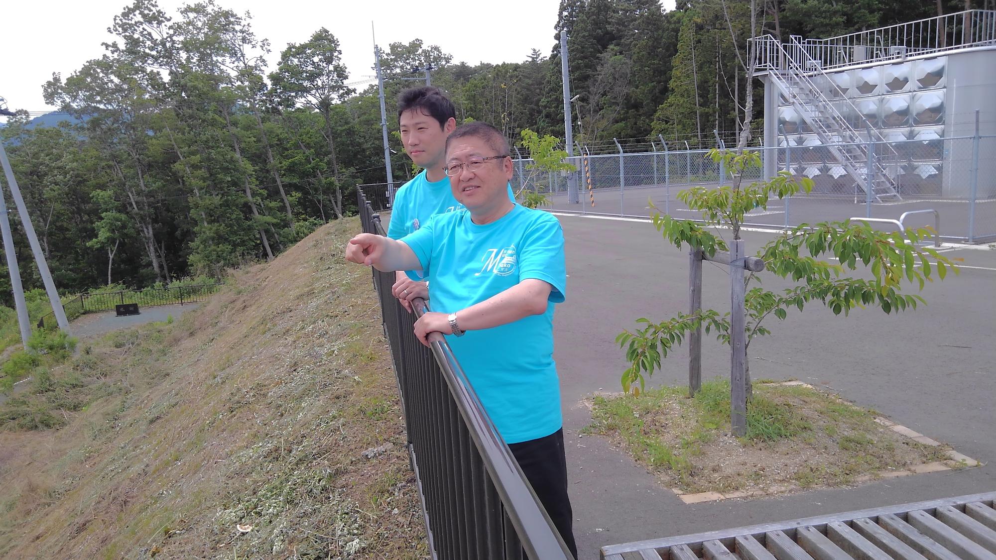青いTシャツを着た市長と男性が、手すりに手を掛け立っている写真