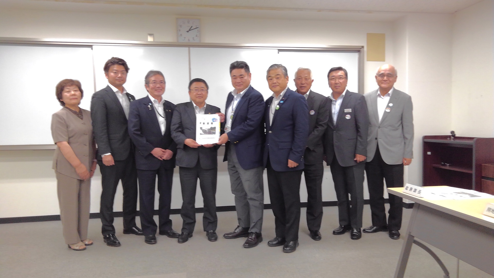 要望書を一緒に持つ市長と男性、関係者の男性6名と女性1名が横一列に並んでいる記念写真