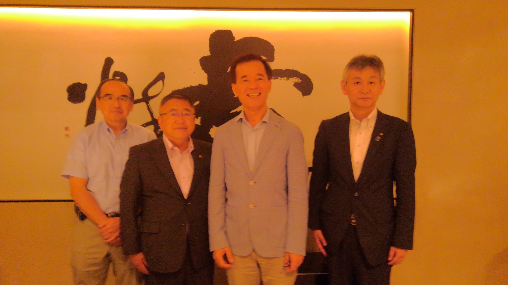 大きな書の額縁が飾られた壁の前で記念撮影をする市長とホンフウ旅行社の方々の写真