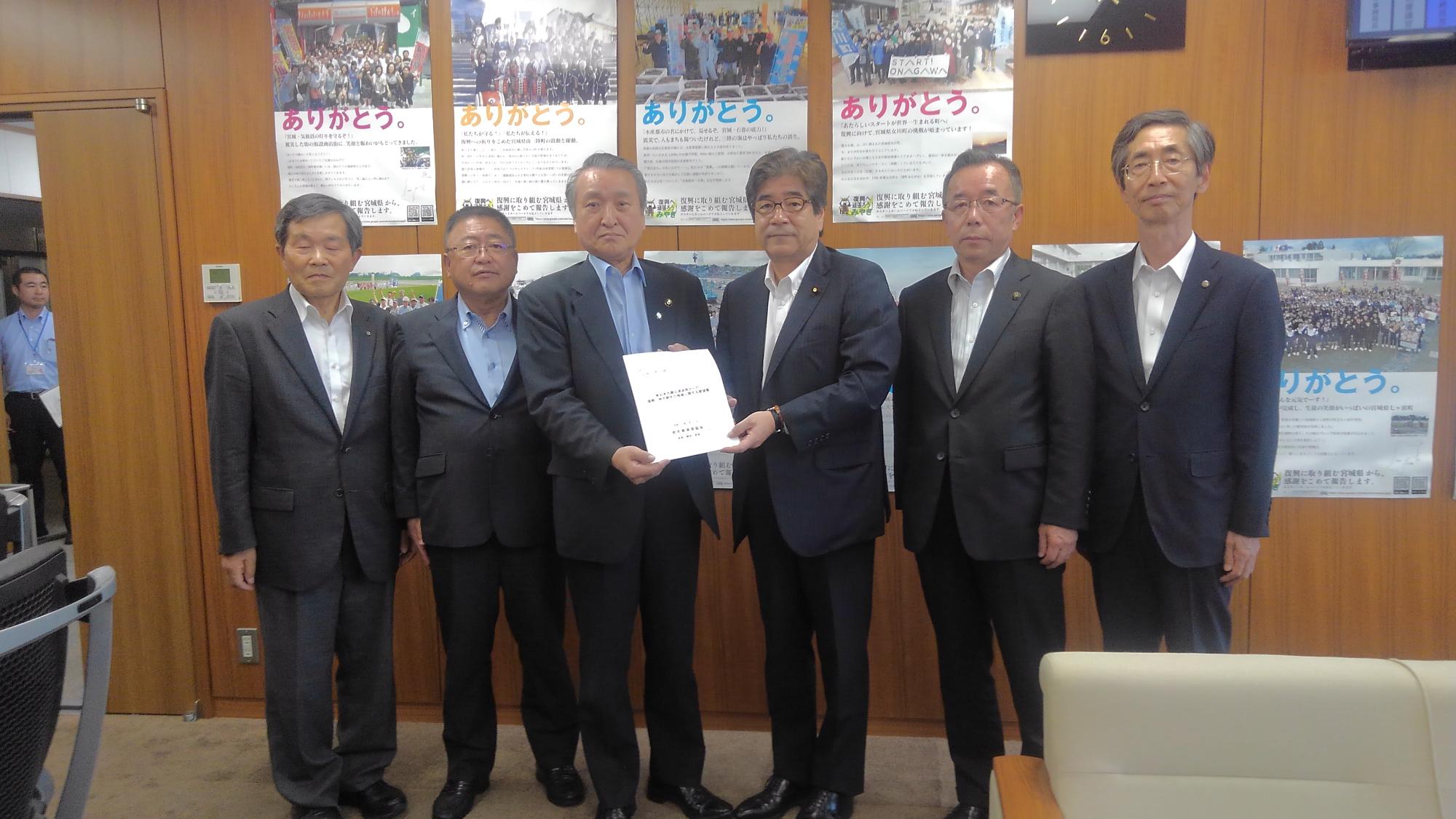 ポスターが貼られた壁の前で、要望書を一緒に持つ男性2名と、市長、男性3名が横一列に並んでいる記念写真